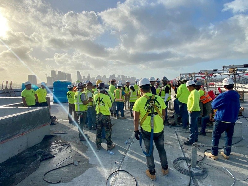 AK Glazing team members on rooftop wait for glazing units to arrive via crane