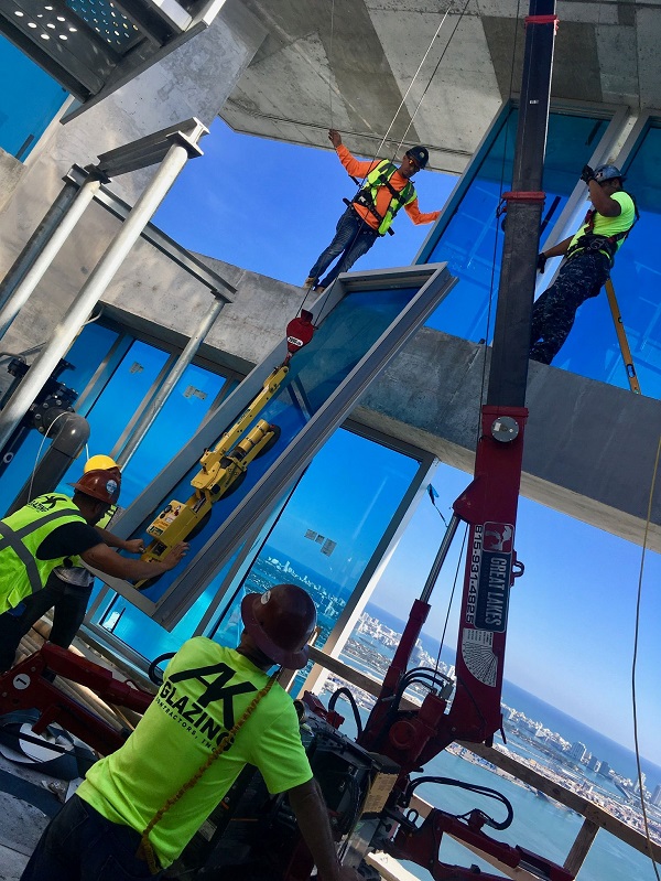 Four glaziers use glass handling unit to lift and install unit on high rise overlooking water