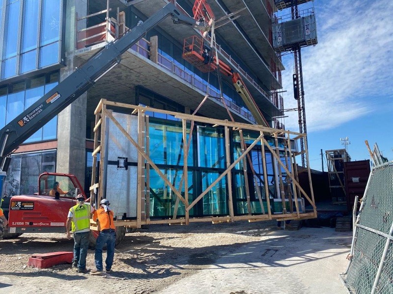 Two glaziers next to crane loaded with glazing units on construction site