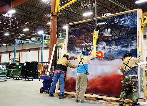 Fabrication personnel at the Vitrum plan use a crane to move a large piece of specialty glass.